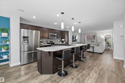 Contemporary kitchen featuring dark wood cabinetry, stainless steel appliances, a mosaic tile backsplash, and a large island with white countertops - 