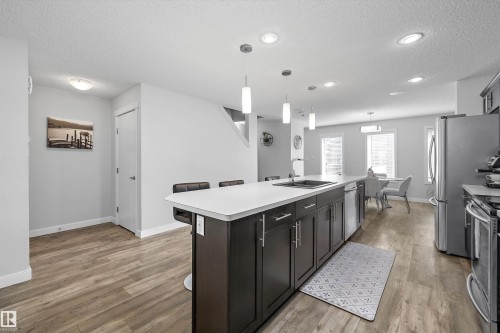 Open-concept kitchen featuring an expansive center island with seating, dark wood-finish cabinetry, and a stainless steel sink - 12305 173A Avenue Nw, Edmonton, AB - Indoor Photo Showing Kitchen With Upgraded Kitchen