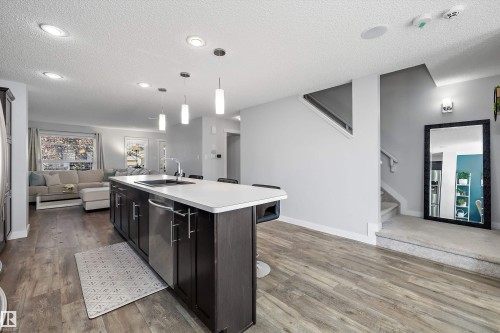 Spacious open-concept living area featuring an island kitchen with a dishwasher, wood-finish flooring, recessed lighting, and a staircase with carpeting - 12305 173A Avenue Nw, Edmonton, AB - Indoor Photo Showing Kitchen