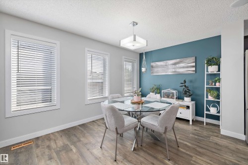 Dining space featuring wood-finish flooring, two window openings with blinds, a prominent blue accent wall, and a square ceiling light fixture - 12305 173A Avenue Nw, Edmonton, AB - Indoor Photo Showing Dining Room