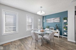 Dining space featuring wood-finish flooring, two window openings with blinds, a prominent blue accent wall, and a square ceiling light fixture - 