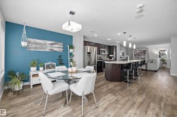 Open-concept living area featuring wood-finish flooring, a kitchen island with seating, dark wood cabinetry, and stainless steel appliances - 