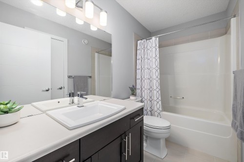 Bathroom featuring a single vanity with a white countertop and dark cabinetry, a large mirror, and a combination bathtub and shower with a white surround - 12305 173A Avenue Nw, Edmonton, AB - Indoor Photo Showing Bathroom
