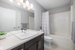 Bathroom featuring a single vanity with a white countertop and dark cabinetry, a large mirror, and a combination bathtub and shower with a white surround - 