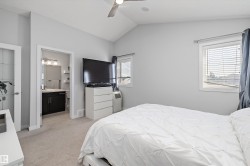 Carpeted room featuring a vaulted ceiling with a flush-mount ceiling fan, two windows with horizontal blinds, and a doorway to a bathroom with a dark wood vanity and light fixture - 