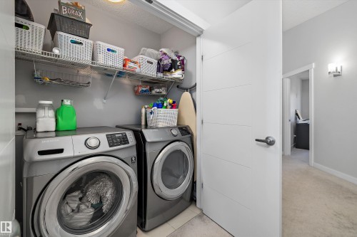Dedicated laundry area featuring front-loading appliances, overhead wire shelving, and neutral wall paint - 12305 173A Avenue Nw, Edmonton, AB - Indoor Photo Showing Laundry Room
