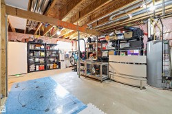Unfinished basement featuring exposed wood joists and structural beams, concrete flooring, and visible utility infrastructure including plumbing and electrical conduits - 