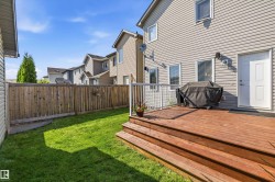 Rear exterior featuring a spacious wood deck with white railings and stairs, a fully fenced yard with a wood privacy fence, and a grassy area - 