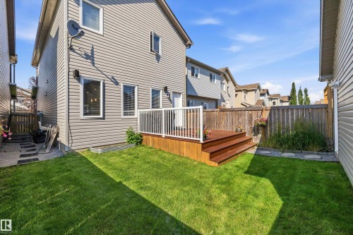 Rear exterior featuring light grey siding, a wood deck with white railings, a green lawn, and a natural wood privacy fence - 12305 173A Avenue Nw, Edmonton, AB - Outdoor With Deck Patio Veranda