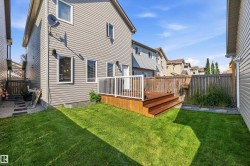 Rear exterior featuring light grey siding, a wood deck with white railings, a green lawn, and a natural wood privacy fence - 
