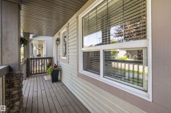Inviting covered porch with composite wood flooring, stone-clad pillars, and a ceiling with horizontal paneling - 
