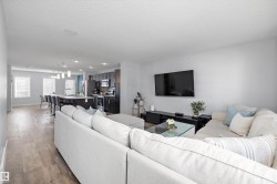 Expansive open-concept living area featuring light wood-finish flooring, recessed lighting, and a modern kitchen with dark cabinetry - 