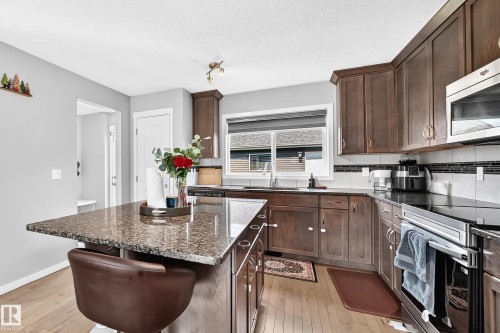 Kitchen featuring wood-finish flooring, dark wood cabinetry, and a central island with a speckled countertop - 5280 21 Avenue Sw, Edmonton, AB - Indoor Photo Showing Kitchen