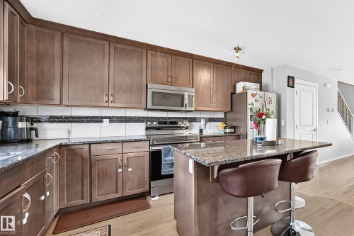 Kitchen featuring wood-finish cabinetry, stainless steel appliances, granite countertops, a tile backsplash, and an island with seating - 5280 21 Avenue Sw, Edmonton, AB - Indoor Photo Showing Kitchen
