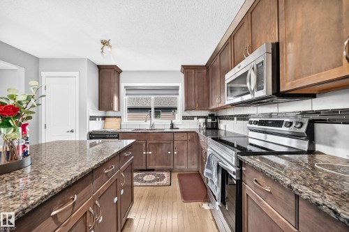 Kitchen featuring dark wood cabinetry, light wood-finish flooring, and granite countertops - 5280 21 Avenue Sw, Edmonton, AB - Indoor Photo Showing Kitchen