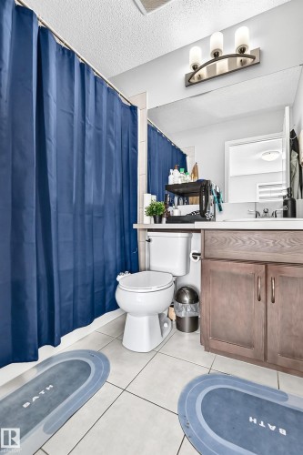 Bathroom featuring a wood-finish vanity with dual doors, a white sink, and a large wall-mounted mirror - 5280 21 Avenue Sw, Edmonton, AB - Indoor Photo Showing Bathroom
