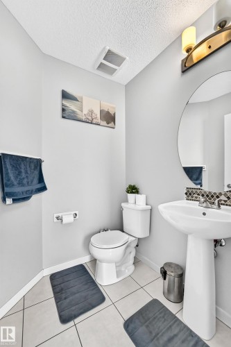 Pedestal sink with mosaic tile backsplash, circular mirror, and wall-mounted light fixture - 5280 21 Avenue Sw, Edmonton, AB - Indoor Photo Showing Bathroom