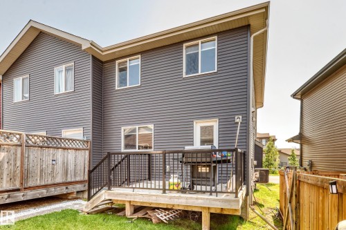 Rear elevation featuring a ground-level deck with black railings, a white egress door, and grey horizontal siding - 5280 21 Avenue Sw, Edmonton, AB - Outdoor With Deck Patio Veranda With Exterior