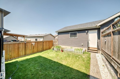 Expansive fenced backyard featuring a manicured lawn, concrete pathway, and private side entrance to the home - 5280 21 Avenue Sw, Edmonton, AB - Outdoor With Exterior