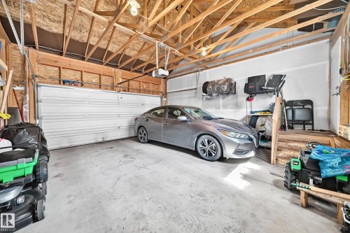 Spacious garage with exposed wood ceiling beams, concrete flooring, overhead lighting, and a white panel garage door - 5280 21 Avenue Sw, Edmonton, AB - Indoor Photo Showing Garage