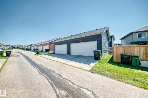 Two-car detached garage with dark blue horizontal siding and white garage doors, featuring a concrete driveway and adjacent grass area - 5280 21 Avenue Sw, Edmonton, AB - Outdoor