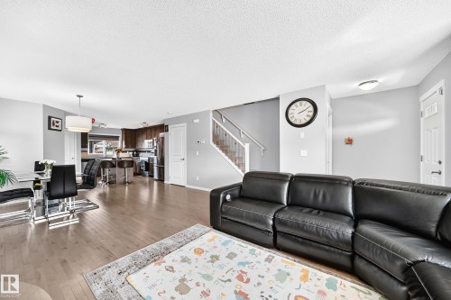 Open-concept living area featuring wood-finish flooring, a contemporary kitchen with dark wood cabinetry and stainless steel appliances, a dining area with a modern light fixture, and a staircase with white railings - 5280 21 Avenue Sw, Edmonton, AB - Indoor Photo Showing Living Room