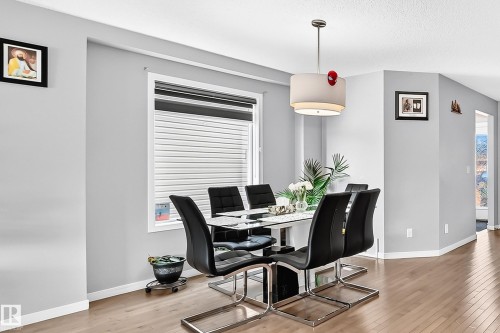 Dining area featuring light wood-finish flooring, a contemporary drum pendant light fixture, and a large window with privacy blinds - 5280 21 Avenue Sw, Edmonton, AB - Indoor Photo Showing Dining Room