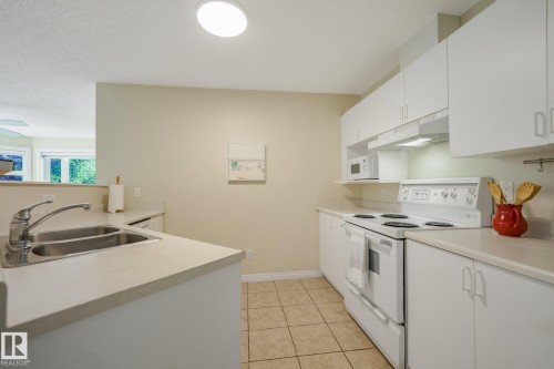 Kitchen featuring white cabinetry, light-toned countertops, a double basin stainless steel sink, and a built-in dishwasher - #206, 9905 112 St Nw, Edmonton, AB - Indoor Photo Showing Kitchen With Double Sink