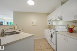 Bright kitchen featuring white cabinetry, a double basin stainless steel sink, and light-toned countertops - 