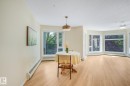 Bright open-concept space featuring lighter tone laminate flooring, a contemporary pendant light fixture, extensive bay windows, a ceiling fan, and baseboard heating - #206, 9905 112 St Nw, Edmonton, AB  - Indoor 