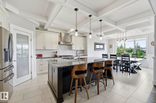Gourmet kitchen and dining area featuring a dark-toned island with seating, pendant lighting, white cabinetry, and stainless steel appliances - 3 Garneau Gate, Spruce Grove, AB - Indoor