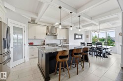Gourmet kitchen and dining area featuring a dark-toned island with seating, pendant lighting, white cabinetry, and stainless steel appliances - 