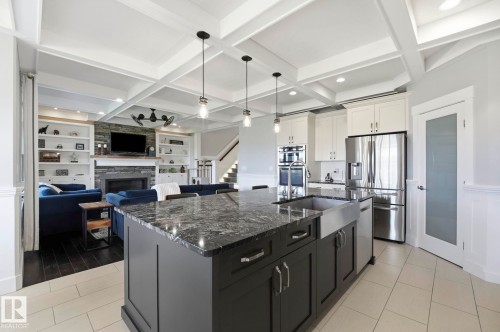 Kitchen island with dark cabinetry, stone countertop, and farmhouse sink - 3 Garneau Gate, Spruce Grove, AB - Indoor Photo Showing Kitchen With Upgraded Kitchen