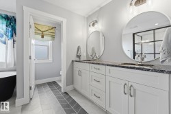 Double vanity featuring white cabinetry, dark stone countertops, and circular mirrors - 