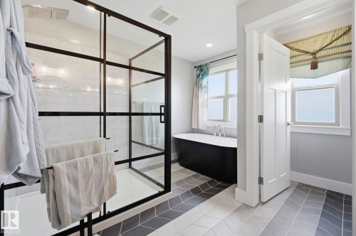 Contemporary bathroom featuring a black-framed glass shower enclosure with white subway tile, a freestanding black soaking tub, and striking chevron-patterned floor tiling in varying shades - 3 Garneau Gate, Spruce Grove, AB - Indoor Photo Showing Other Room