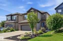 Contemporary exterior with stone accents and horizontal siding, featuring a two-car garage, established front landscaping, a bright blue entry door, and a paved driveway - 