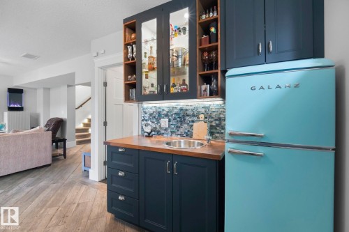 Built-in wet bar featuring dark cabinetry, a wood-finish countertop, a stainless steel sink, and a colorful tiled backsplash - 3 Garneau Gate, Spruce Grove, AB - Indoor