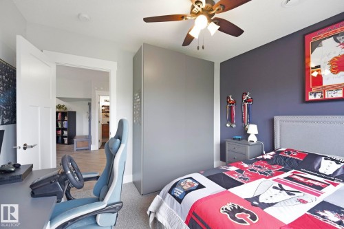 Carpeted bedroom featuring a ceiling fan with integrated lighting, a paneled door with brushed nickel hardware, and a gray upholstered headboard with nailhead trim - 3 Garneau Gate, Spruce Grove, AB - Indoor Photo Showing Bedroom