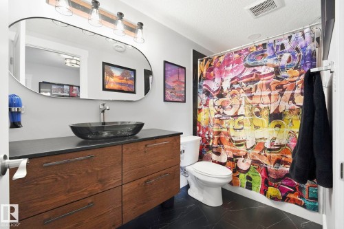Bathroom featuring wood-finish vanity with a dark countertop, vessel sink, and an oval mirror - 3 Garneau Gate, Spruce Grove, AB - Indoor Photo Showing Bathroom