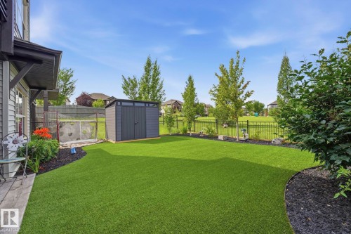 Expansive backyard featuring artificial turf, a dark grey storage shed, decorative black mulch landscaping, a black metal fence, and mature trees - 3 Garneau Gate, Spruce Grove, AB - Outdoor With Backyard