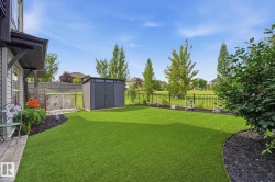 Expansive backyard featuring artificial turf, a dark grey storage shed, decorative black mulch landscaping, a black metal fence, and mature trees - 
