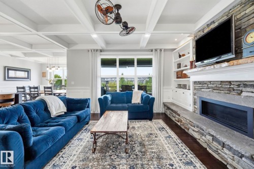 Living area featuring a coffered ceiling, wood-finish flooring, and a stacked stone fireplace with a stone hearth - 3 Garneau Gate, Spruce Grove, AB - Indoor Photo Showing Living Room With Fireplace