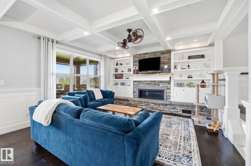 Spacious living area featuring a stone fireplace with a wood mantle, built-in shelving, wood-finish flooring, and a coffered ceiling - 3 Garneau Gate, Spruce Grove, AB - Indoor Photo Showing Living Room With Fireplace
