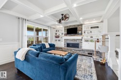 Spacious living area featuring a stone fireplace with a wood mantle, built-in shelving, wood-finish flooring, and a coffered ceiling - 