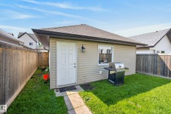 Detached auxiliary building with tan vinyl siding, a brown shingle roof, and a white entry door - 