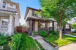 Two-story residence featuring light-colored siding with dark trim, a covered front porch with dark railings, and a concrete pathway leading to the entrance - 