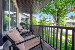 Covered front porch featuring a dark wood-finish railing, dark wood-finish ceiling, and large windows with white trim - 