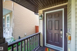 Covered entry porch featuring a paneled front door with dark trim, an exterior lantern light, and a dark railing with vertical balusters - 