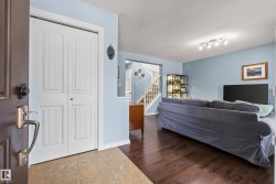 Entryway with ceramic tile flooring opening to a living area featuring wood-finish flooring, light blue wall paint, and a staircase with white risers and handrails - 
