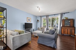 Spacious living area featuring rich wood-finish flooring, light blue wall paint, and substantial windows with natural light - 